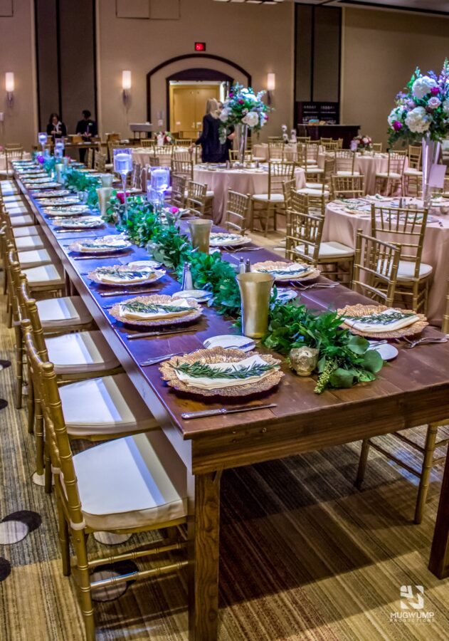 Long wooden tables set up for a community dinner with gold accent decorations.